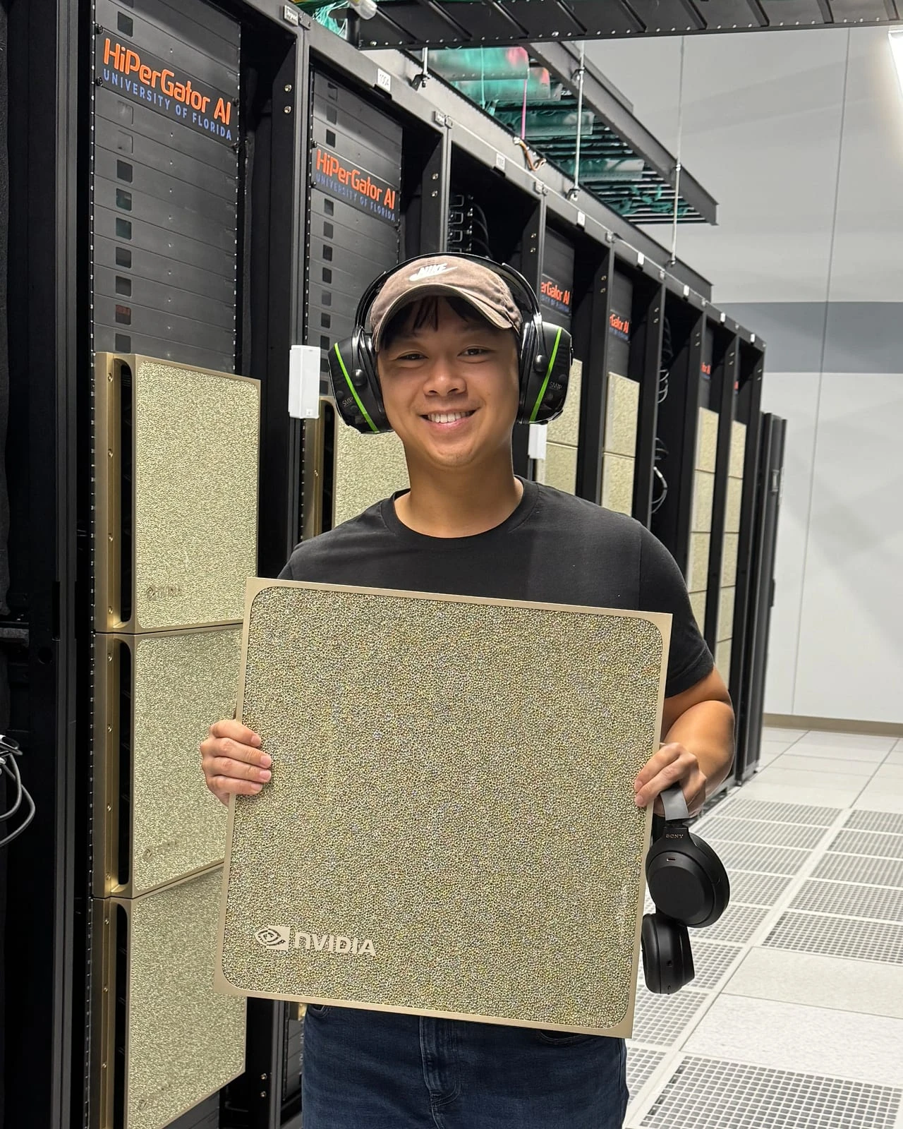 Standing in a data centre aisle in ear defenders, holding an NVIDIA server panel